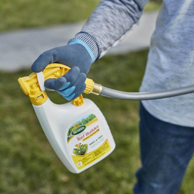 Person wearing blue gloves holding hose attachment connected to liquid turf builder sprayer for lawn care tasks