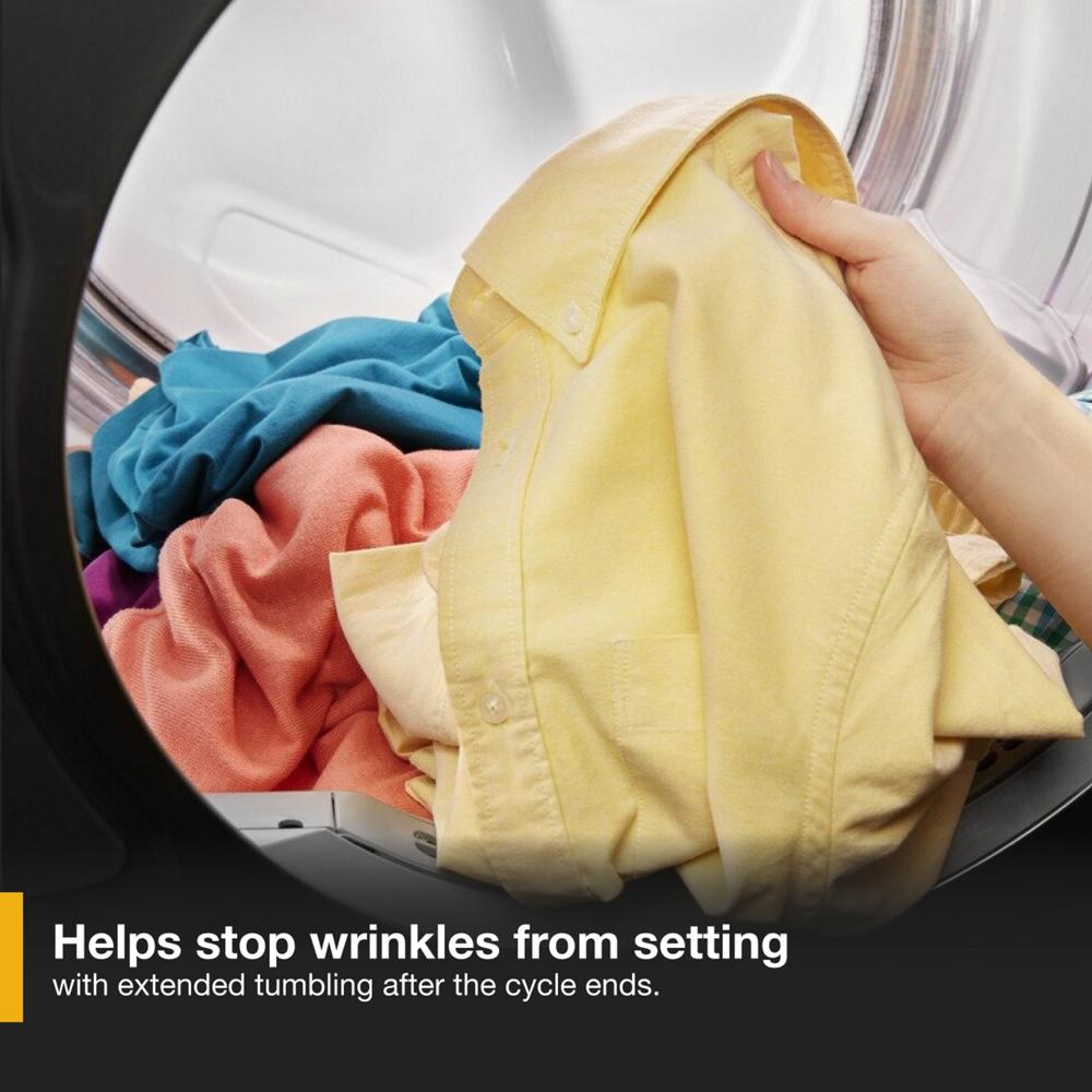 Hand removing yellow shirt from front load heat pump dryer with colorful clothes inside drum in laundry setting