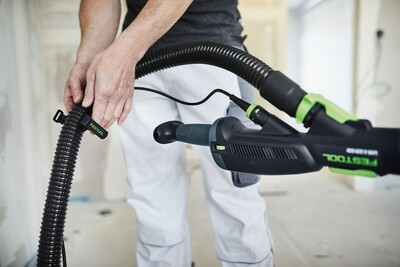 Person attaching a Festool hose clip to a black and green power tool hose in a home improvement setting.