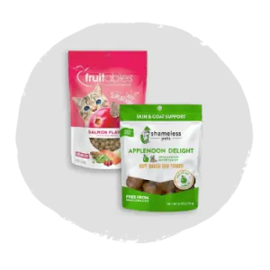 Two colorful pet treat pouches, one featuring a salmon flavor for cats with a playful kitten image, the other a skin and coat support treat for dogs featuring apple scent, displayed on a soft gray circular background.