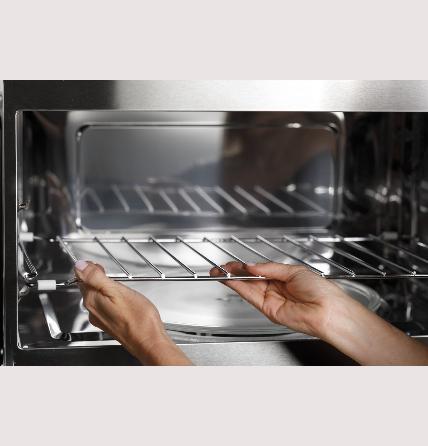 Hands placing metal rack inside stainless steel convection over-the-range microwave in kitchen appliances setting