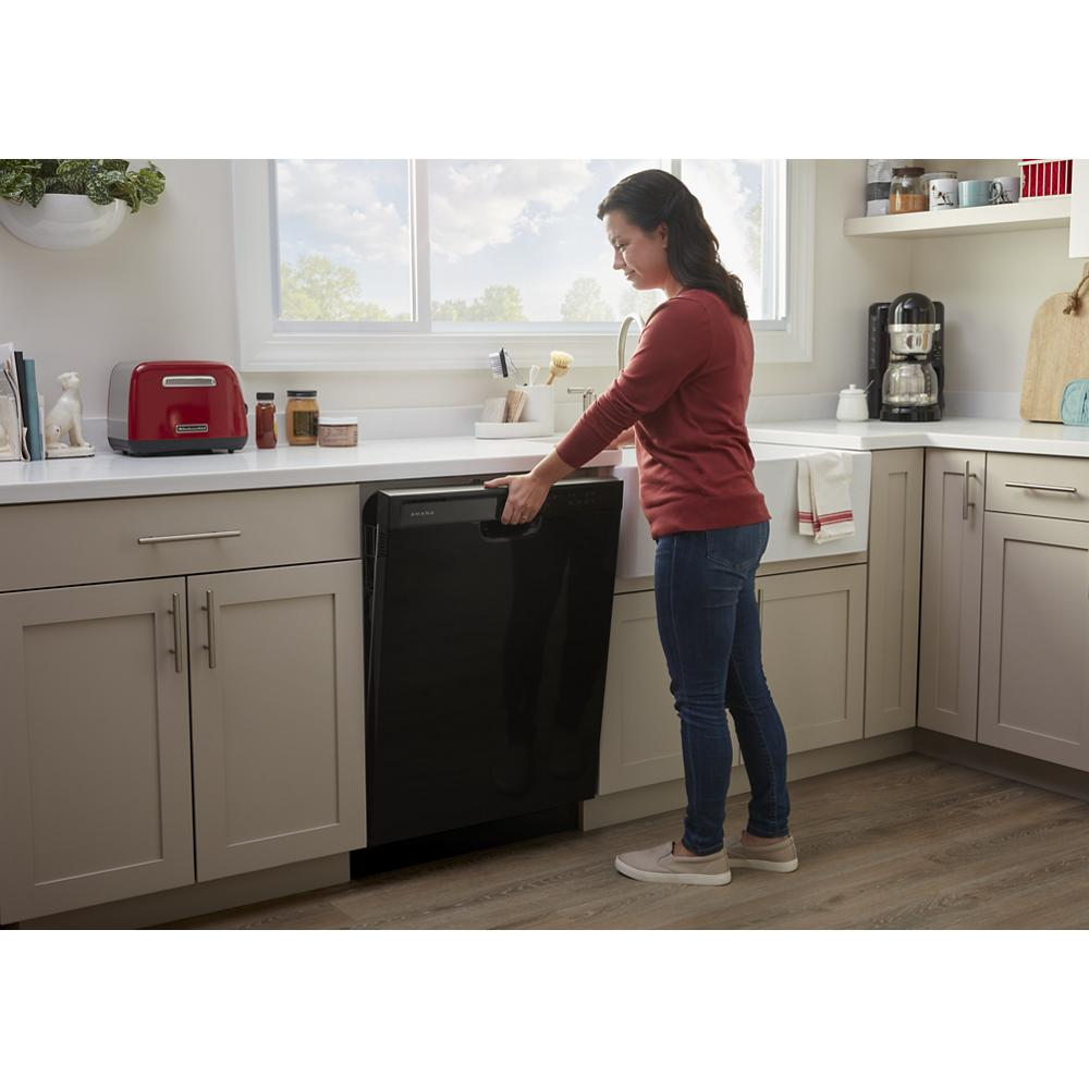 Woman loading black built-in dishwasher in bright modern kitchen with beige cabinets and hardwood floor
