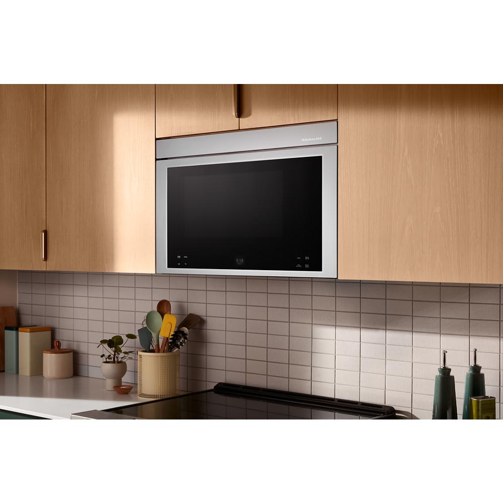 Built-in stainless steel over-the-range microwave with black glass door installed in light wood kitchen cabinetry