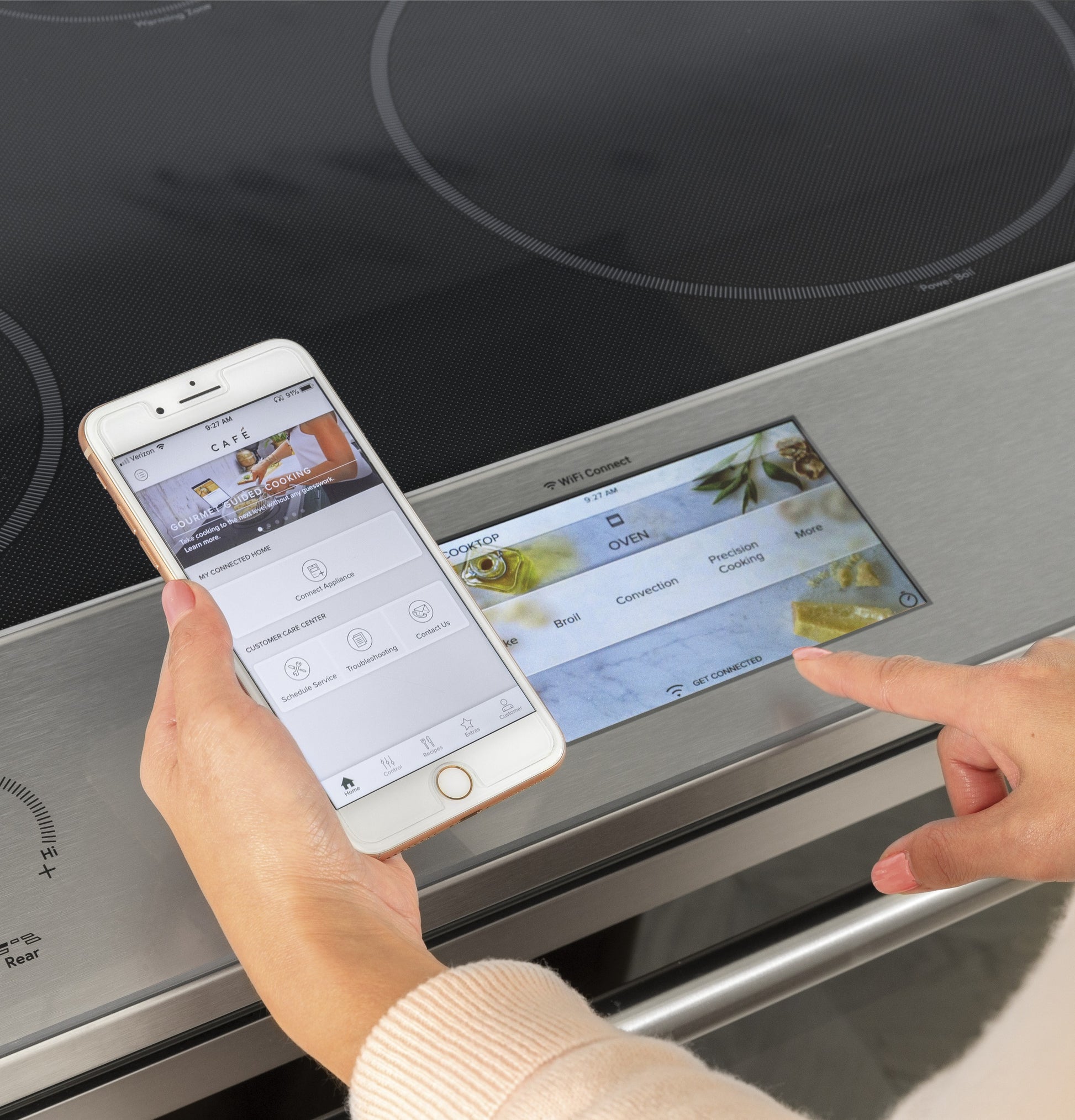 Person using smartphone app to remotely control induction cooktop settings on stainless steel smart range panel