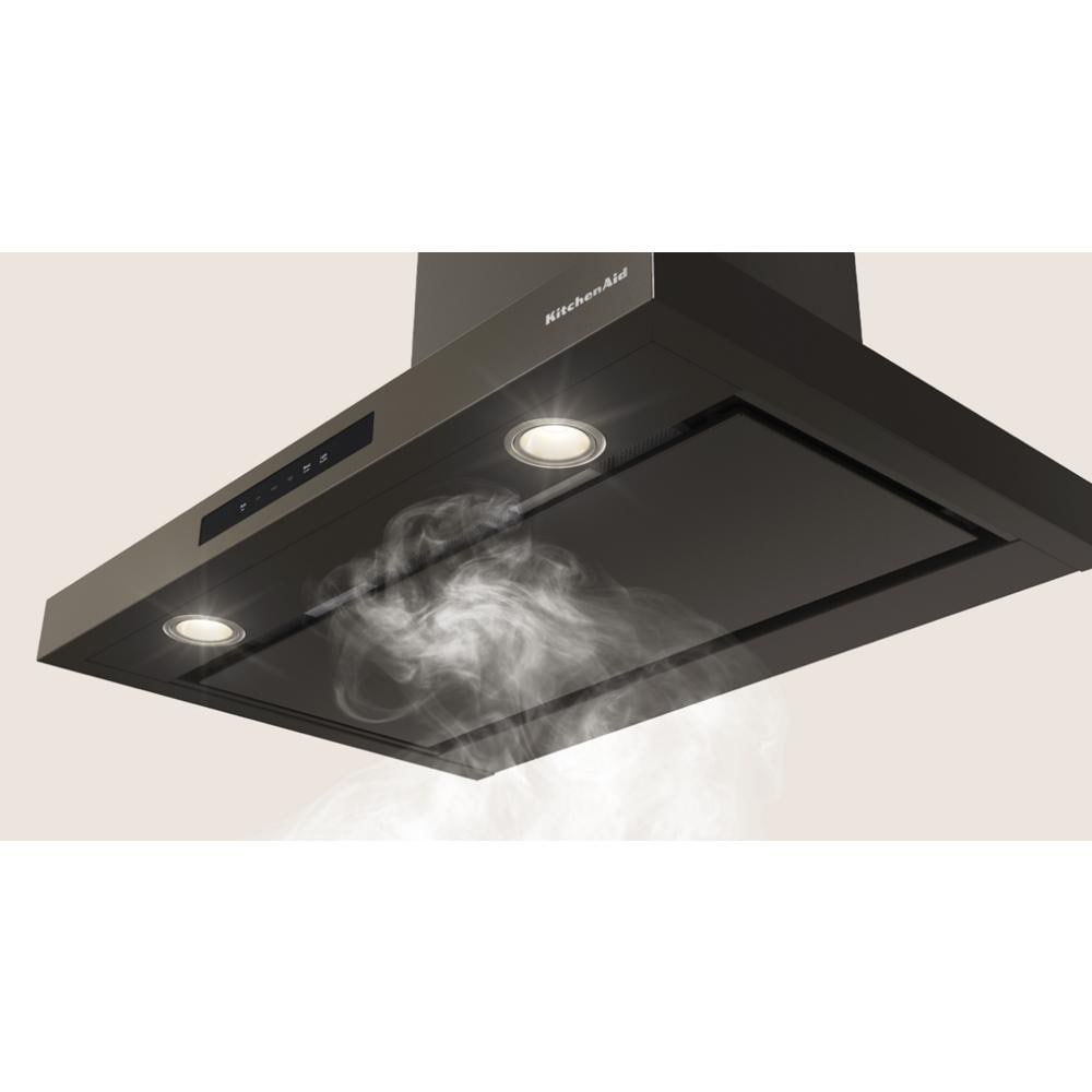 Matte black wall-mounted canopy hood with LED lights and active ventilation clearing kitchen smoke efficiently