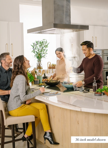 People enjoying cooking and dining together in a modern kitchen featuring a stainless steel island range hood from Thermador.