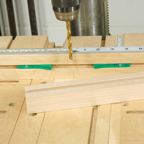 Drill bit positioned over wooden board on a workbench with measuring ruler for precise woodworking tasks