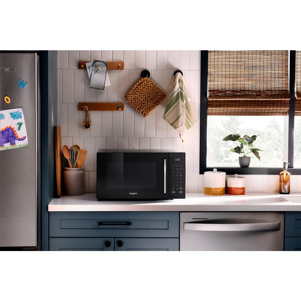 Black multifunctional microwave with digital control on kitchen countertop near window with blinds and utensils