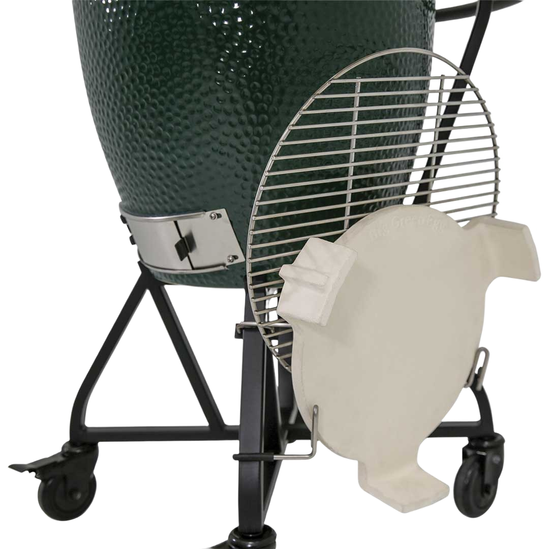 Black steel utility rack attached to outdoor ceramic grill holding a metal cooking grid and ceramic baking stone accessory