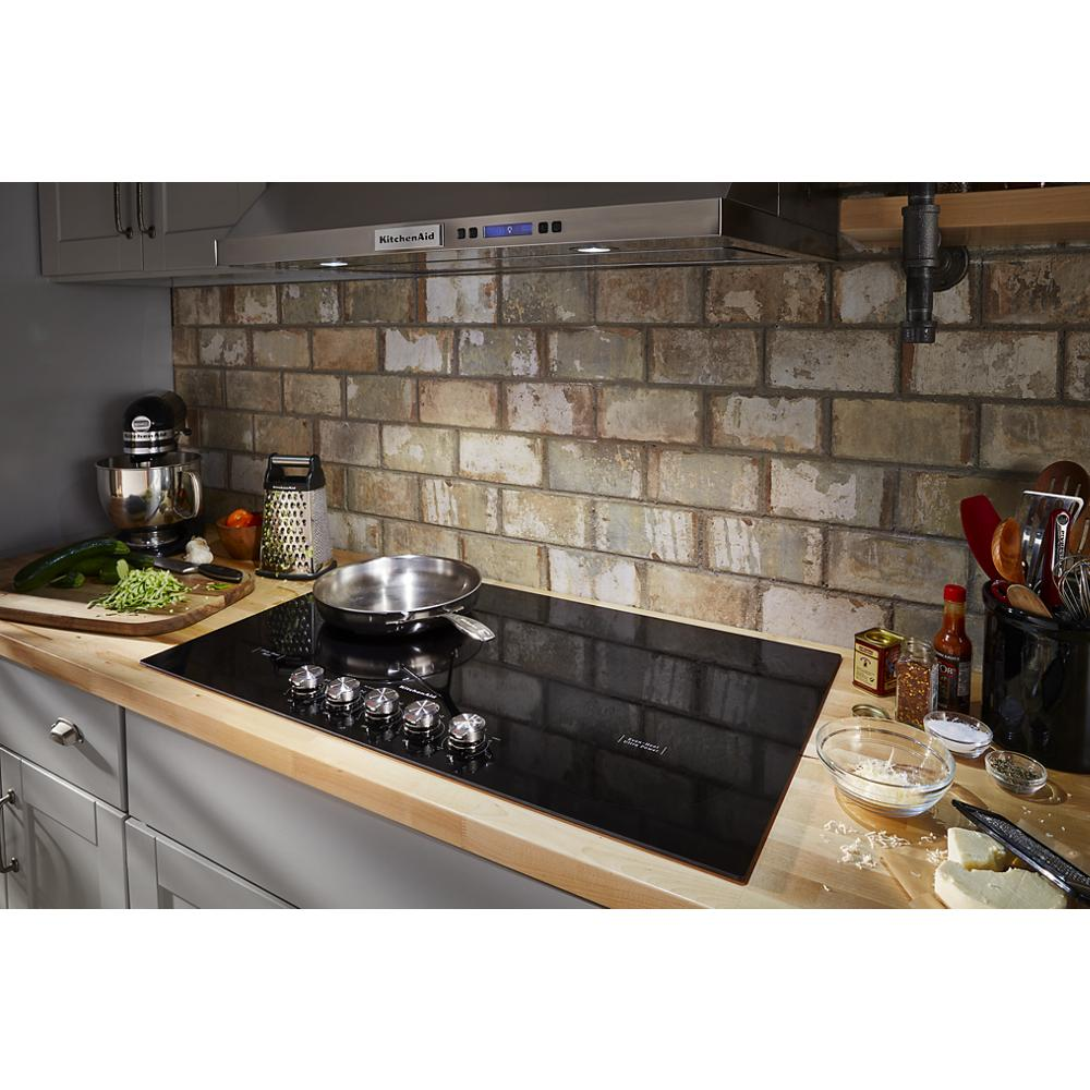 Black electric cooktop with five knob controls on wooden countertop in rustic kitchen setting with brick backsplash