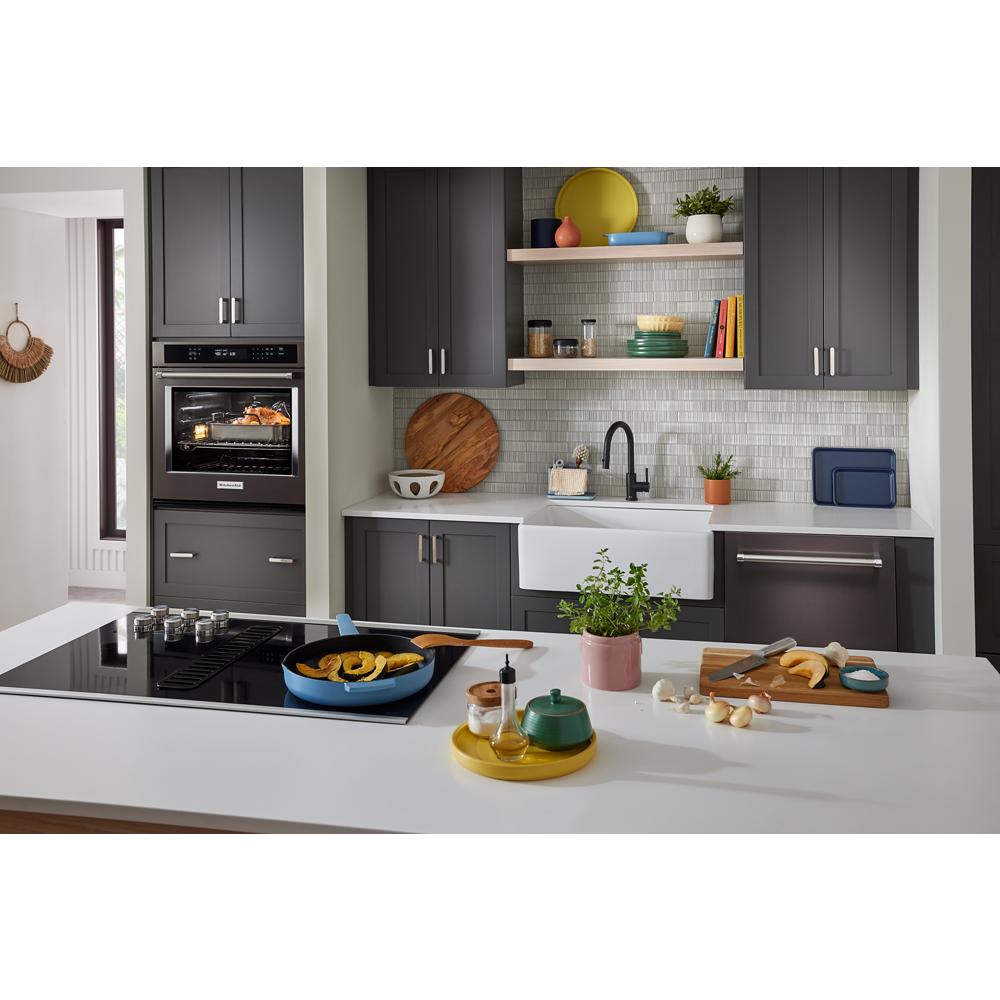 Modern kitchen with dark gray cabinetry, built-in oven roasting chicken, farmhouse sink, and cooking island with stove and cutting board