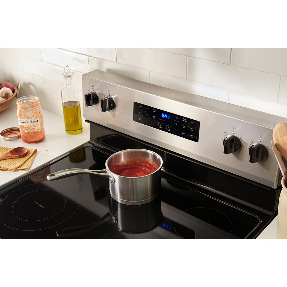 Stainless steel 30-inch electric range with digital control panel and induction cooktop heating a saucepan of sauce