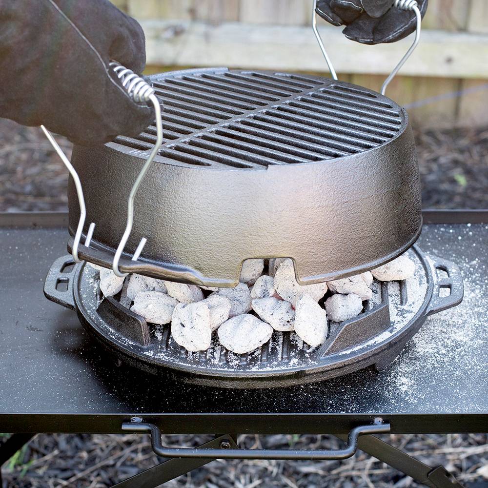 Cast iron grill with detachable handles being lifted off charcoal tray on outdoor cooking table in kitchenware collection