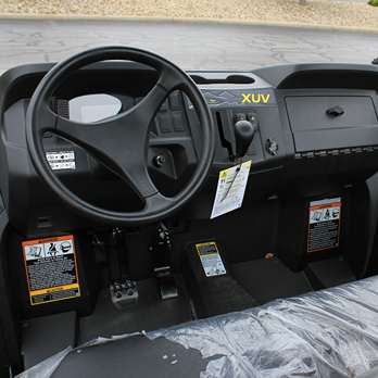 Interior cabin view of John Deere Custom XUV590M with steering wheel, pedals, gear shift, and control panel in camo style