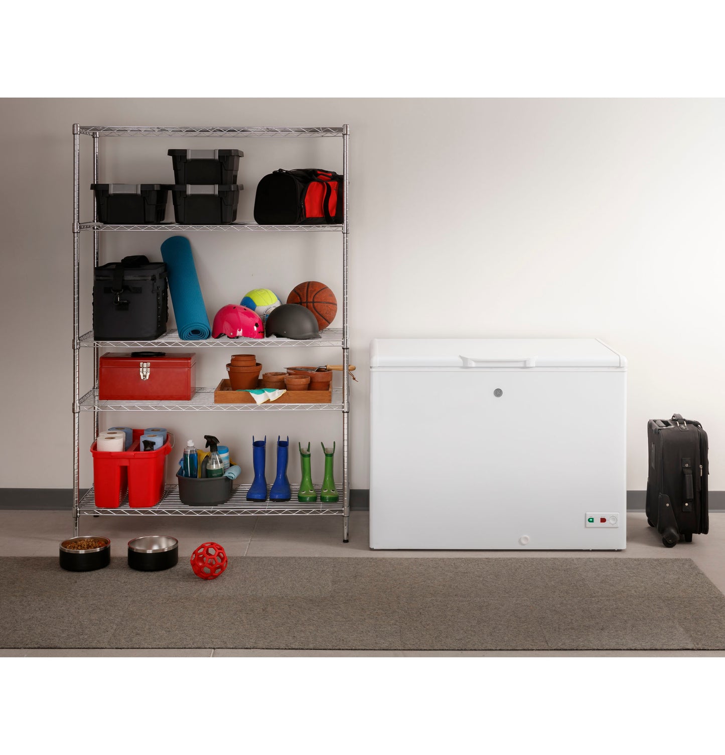 White chest freezer in home setting next to metal shelving with sports gear, gardening pots, and storage bins nearby