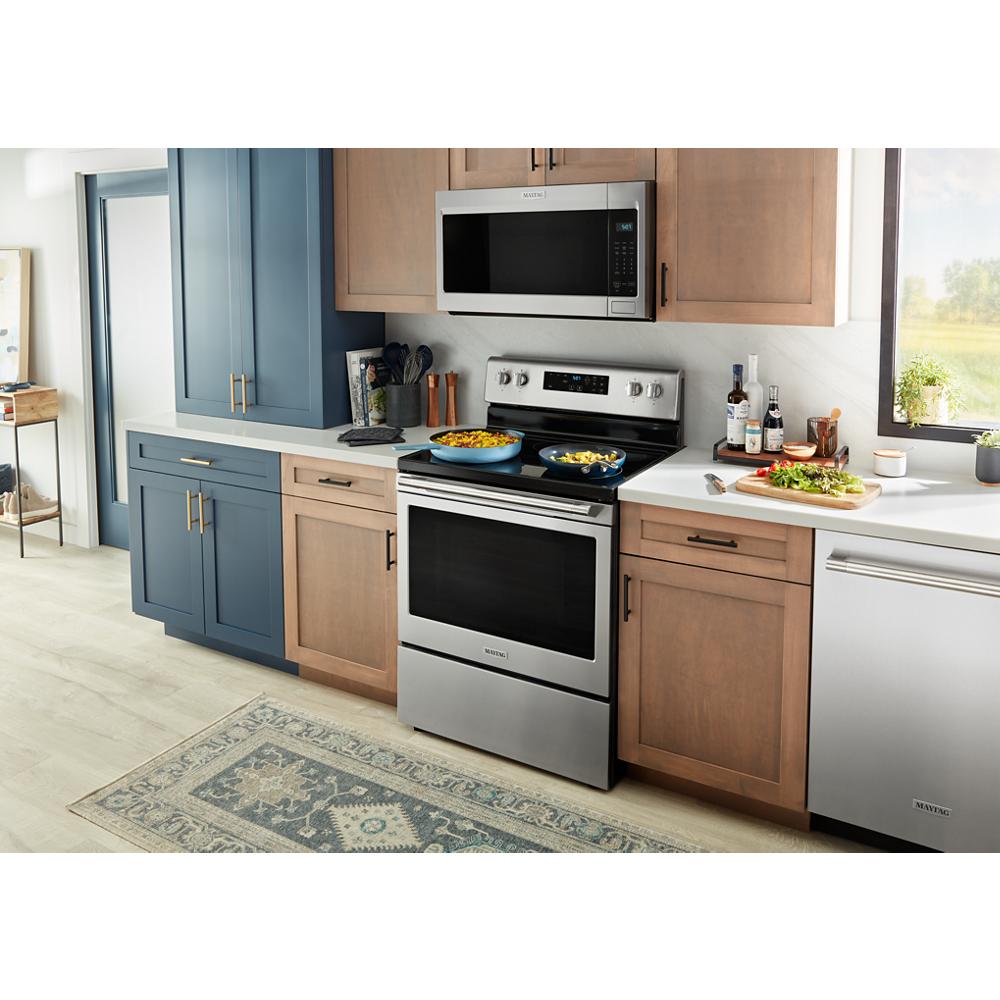 Stainless steel electric range cooking meals in modern kitchen with blue and wood-tone cabinets and natural light