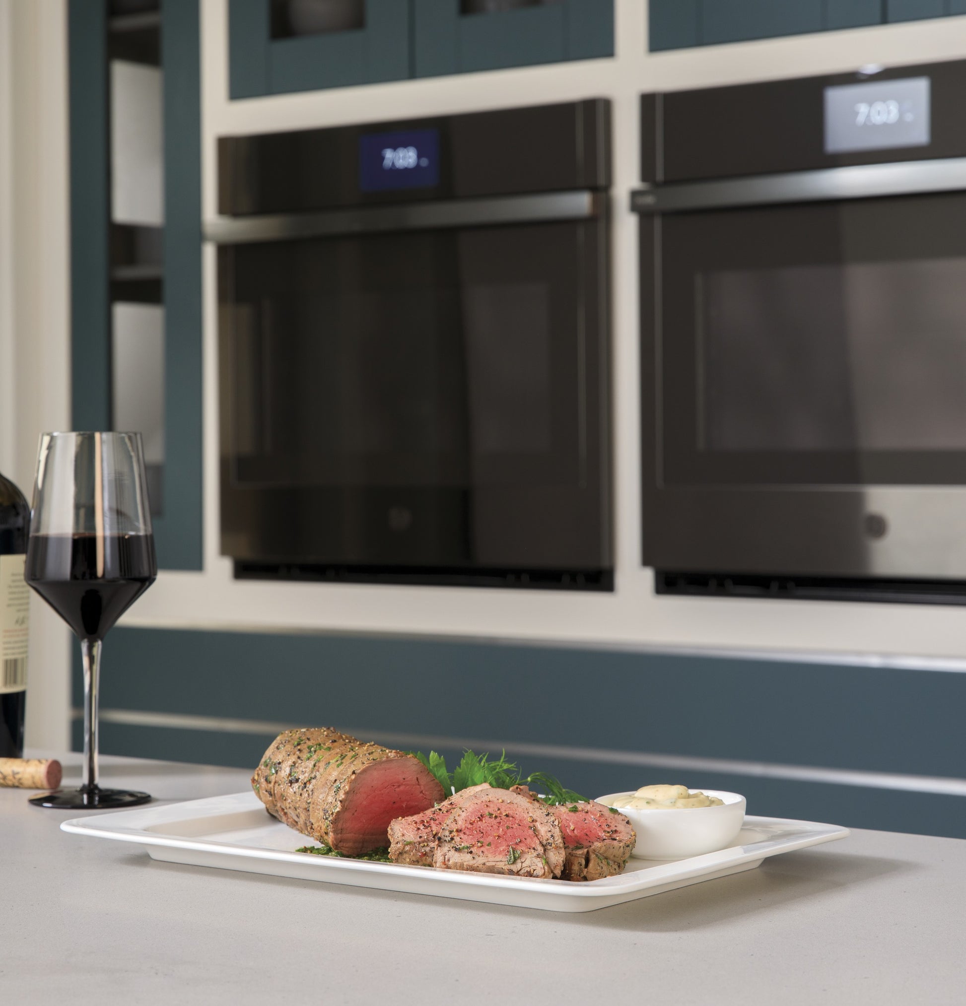 Modern kitchen with two built-in black convection wall ovens and a plate of sliced roast beef and mashed potatoes on counter