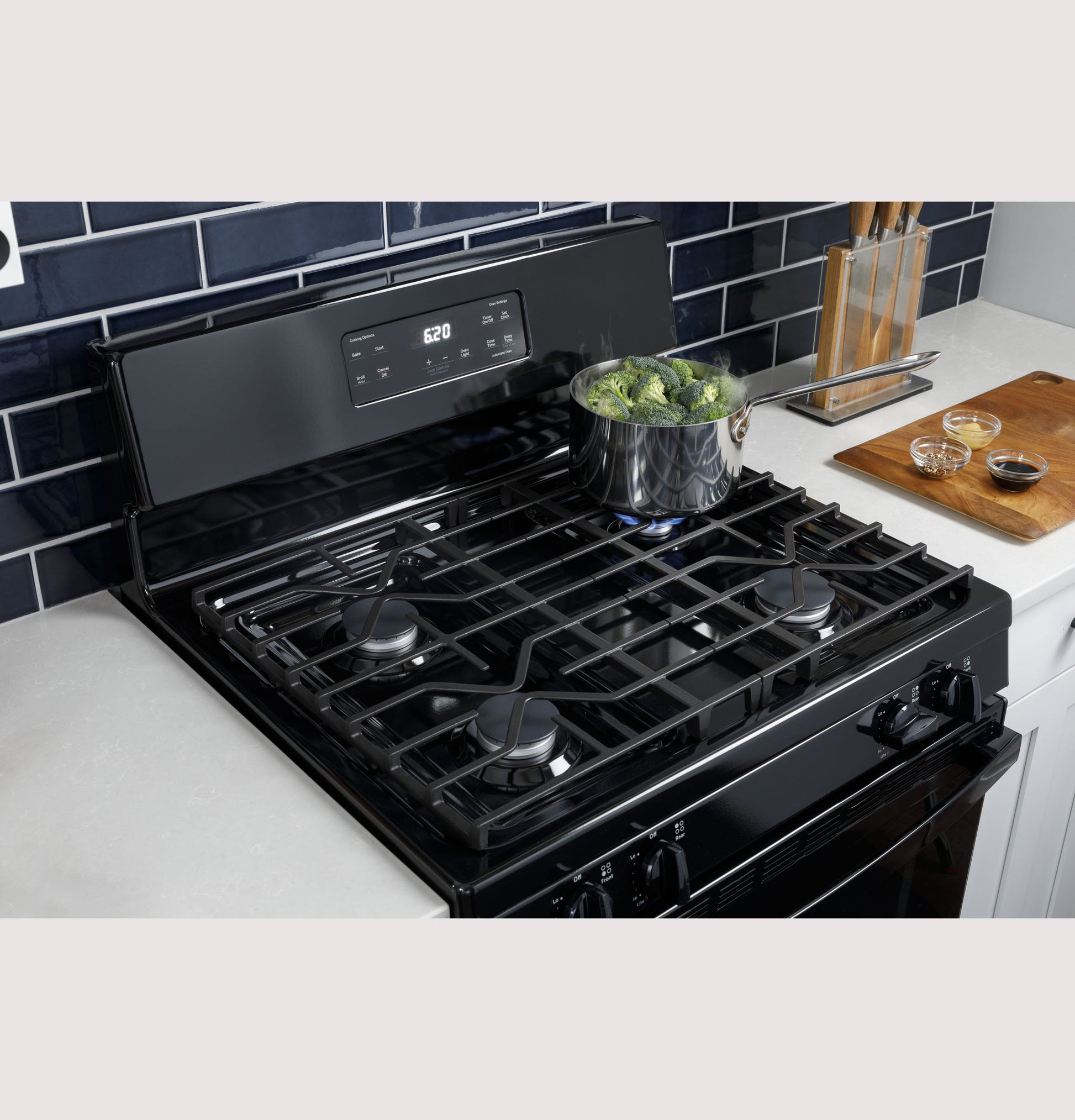Sleek black gas range with five burners and digital control panel cooking broccoli in a modern kitchen setting
