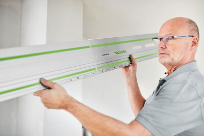 Man installing a long Festool guide rail on a wall for woodworking and home improvement projects