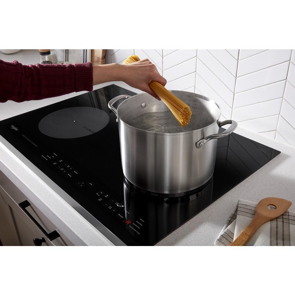 Hand adding spaghetti to boiling water in large stainless steel pot on black induction cooktop in modern kitchen