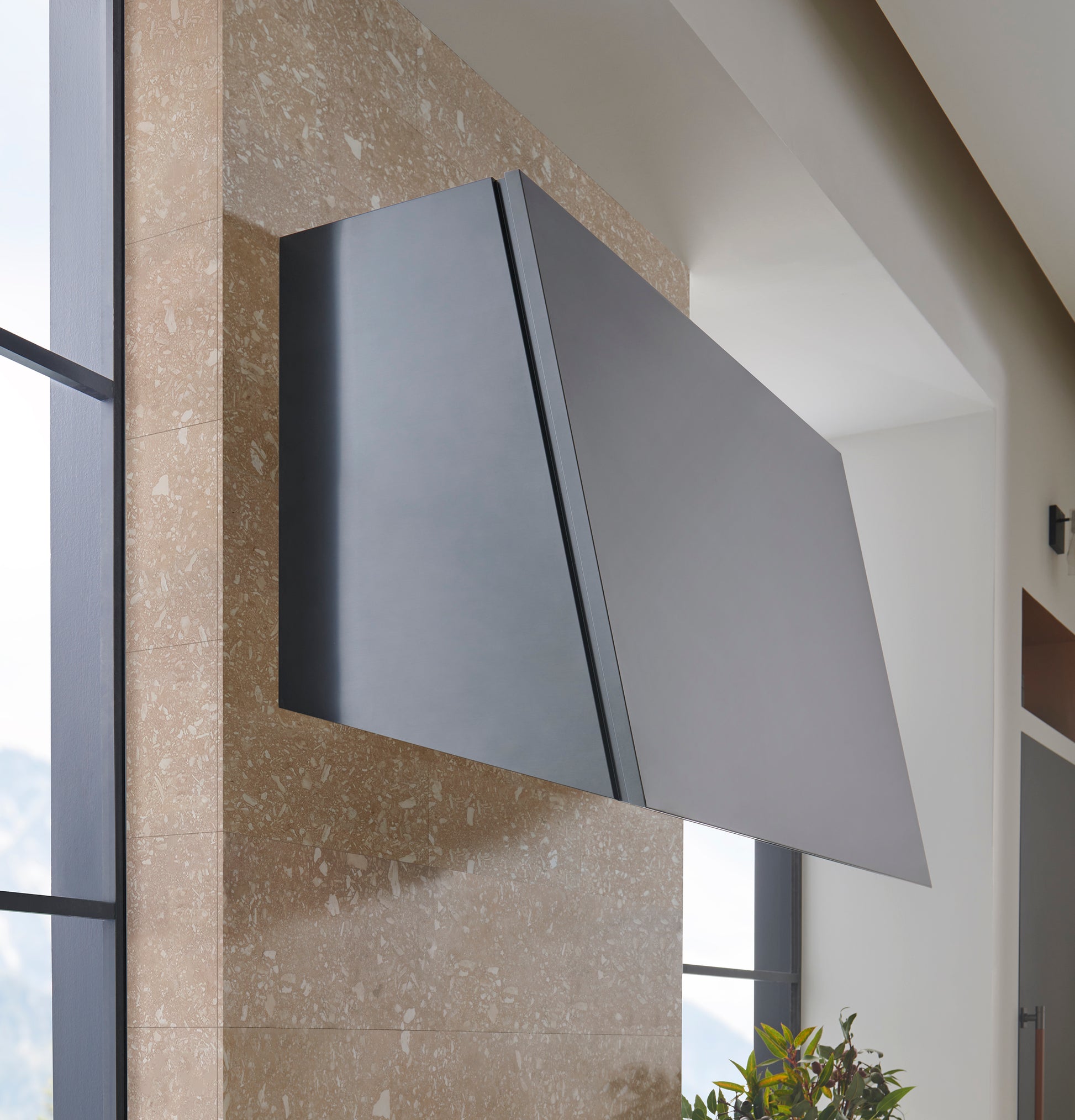 Sleek titanium range hood mounted on stone wall with angled modern design in kitchen appliances collection