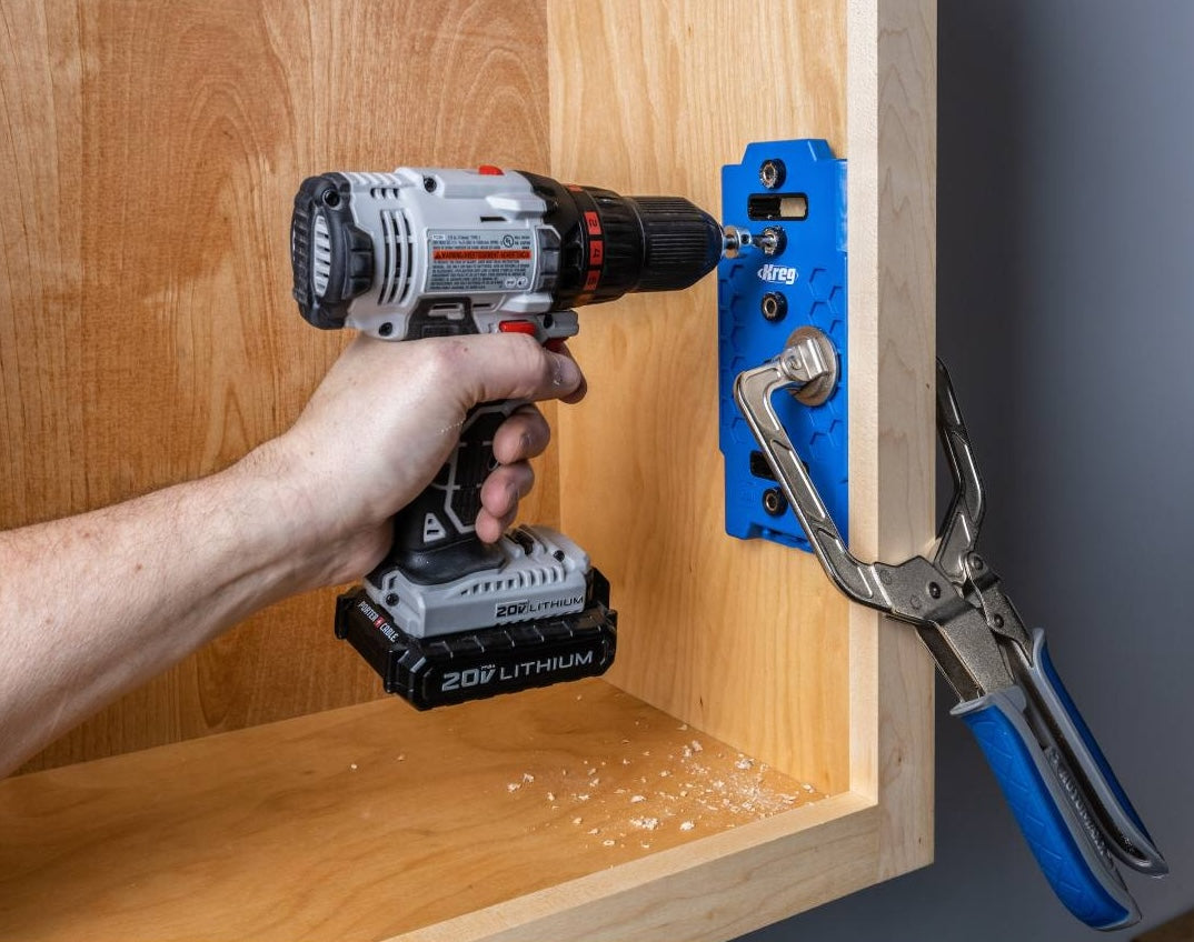 Hand holding cordless drill using blue Kreg shelf pin jig clamped to wood for precise hole drilling in home improvement project