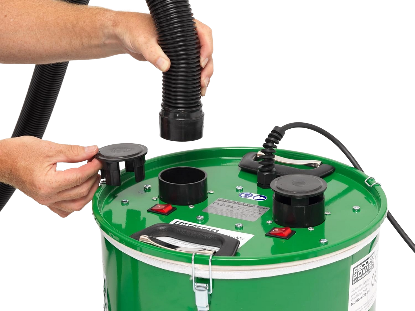 Hands attaching a flexible black hose to the green drum top of a cyclonic dust extractor used for woodworking tools and dust collection tasks.