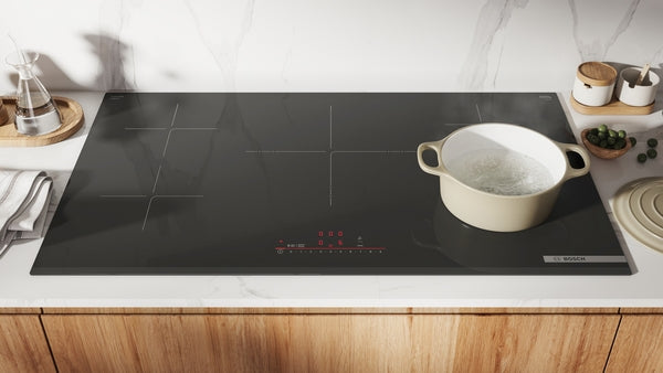 Modern black induction cooktop with four cooking zones and a white pot simmering water on sleek kitchen countertop