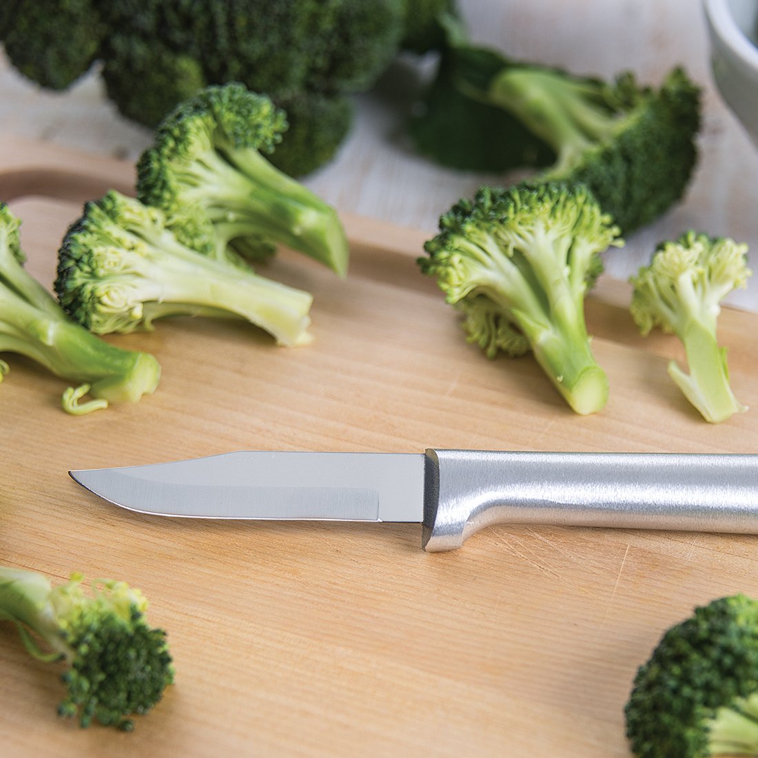Sharp paring knife with sleek metal handle and stainless steel blade on wooden board with broccoli pieces in kitchenware collections