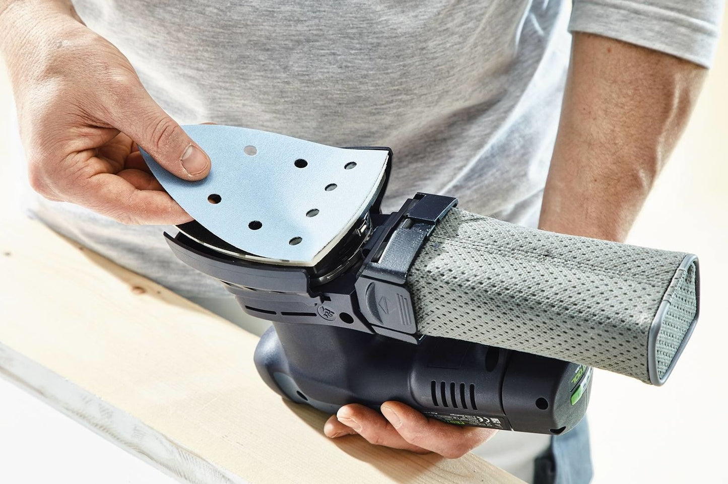 Person attaching sanding pad to cordless delta sander, part of Festool cordless power tools collection