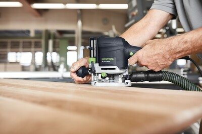 Person operating a Festool woodworking router with dust extraction on wood in a professional workshop setting