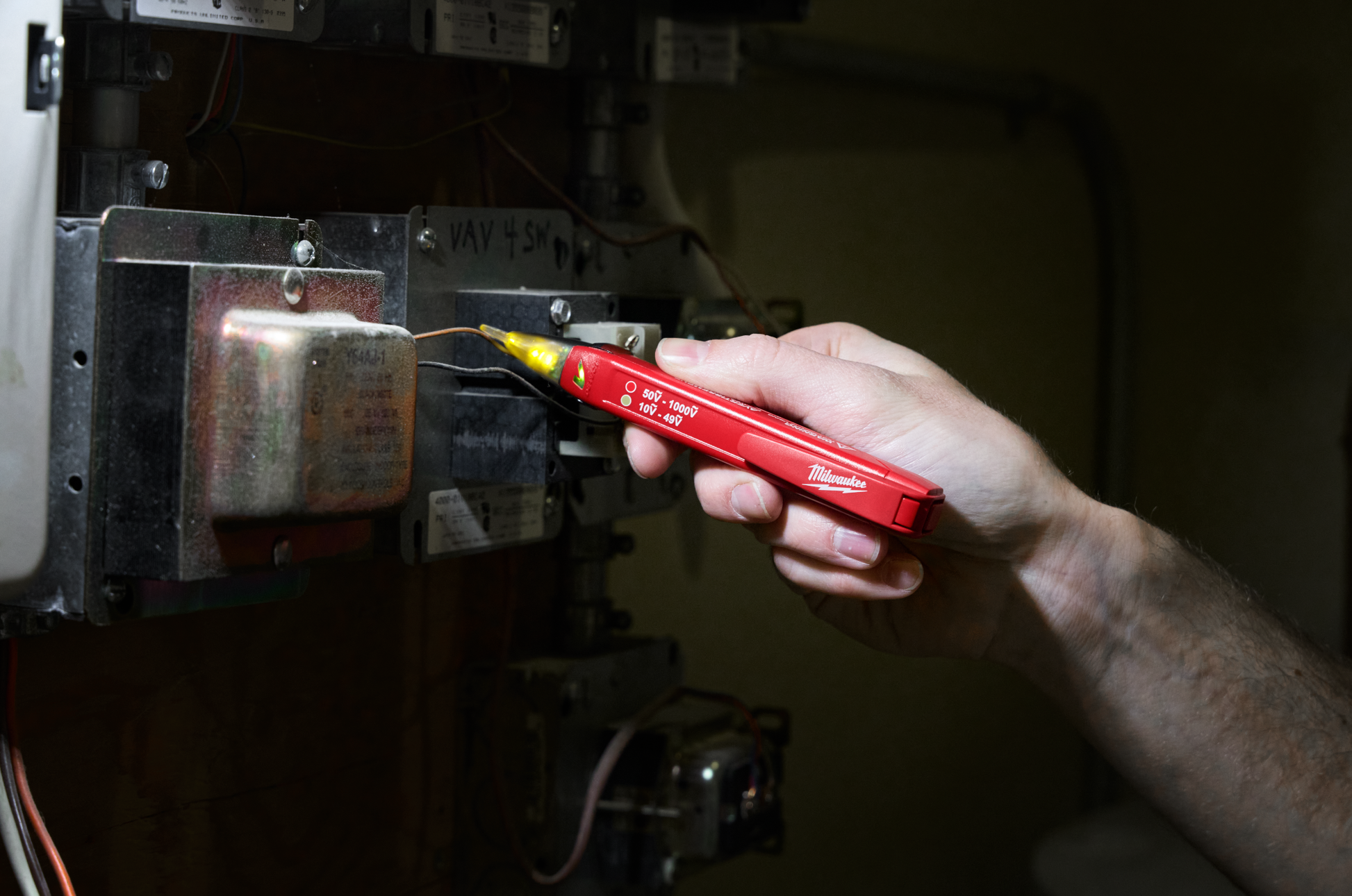 Hand holding a red voltage tester pen detecting electrical current in a circuit panel for home improvement tasks
