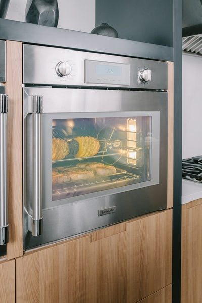 Thermador stainless steel single wall oven with right side door cooking rotisserie chicken and baked goods in modern kitchen