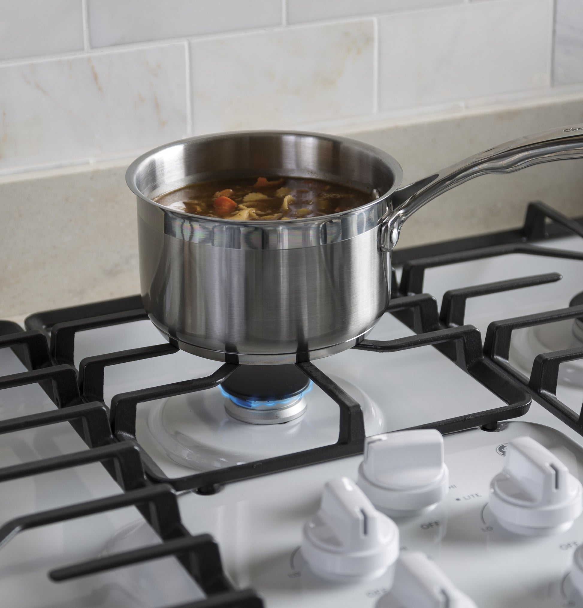 Stainless steel saucepan simmering soup on a burner of a 36-inch built-in gas cooktop with dishwasher-safe grates