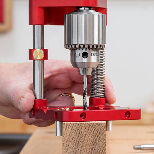 Red drill guide with height adjustment spring and clamp drilling into wood for precise holes in tool and power accessories collections