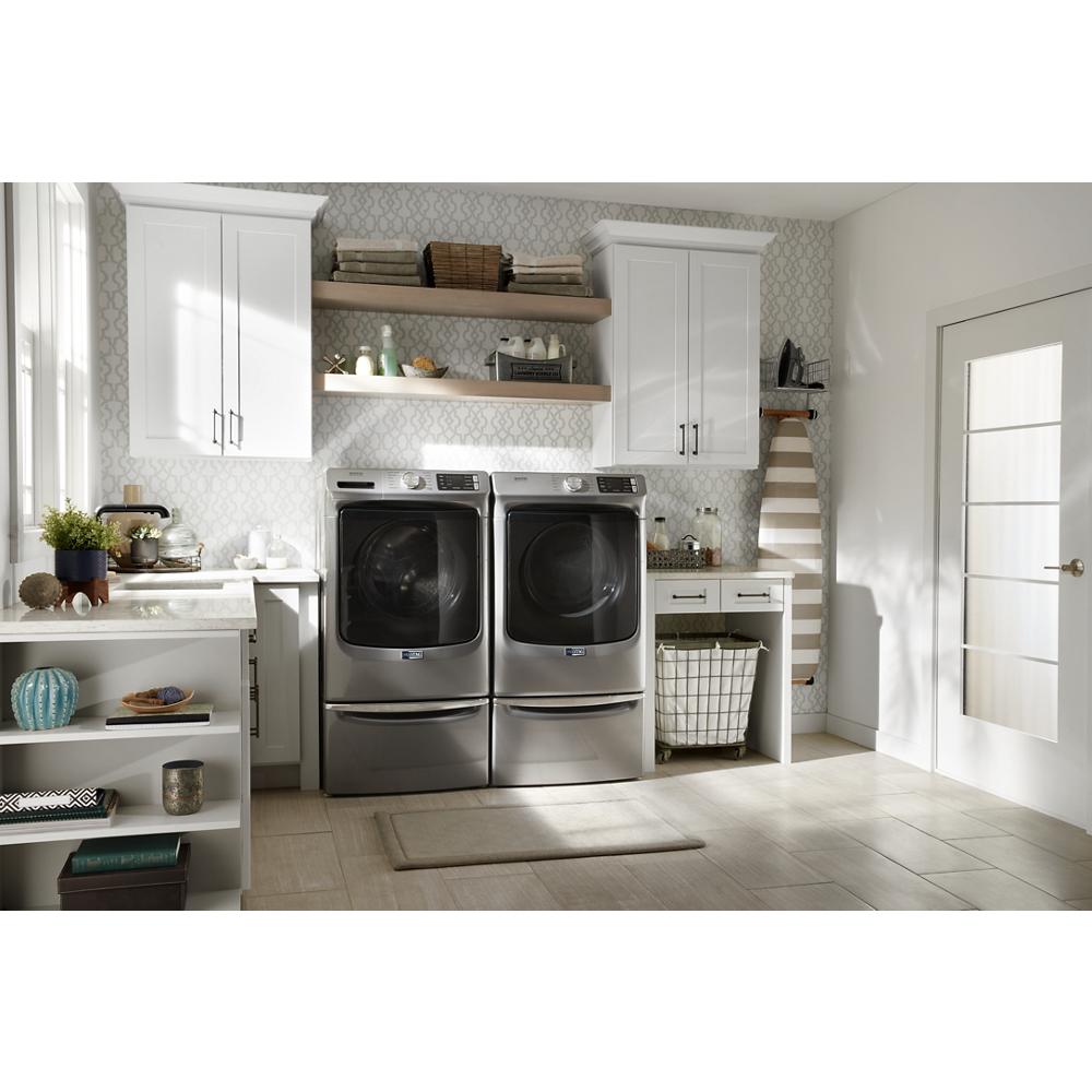 Laundry room featuring front load stainless appliances on 15.5" pedestals with storage, white cabinetry, and decorative shelving