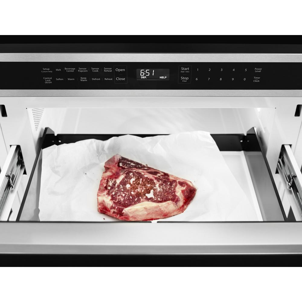 Stainless steel under-counter microwave drawer with digital control panel, open showing a piece of raw steak inside