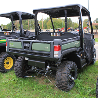 Rear view of green John Deere utility vehicle with roof, large tires, cargo bed, and 4x4 capability on grassy terrain