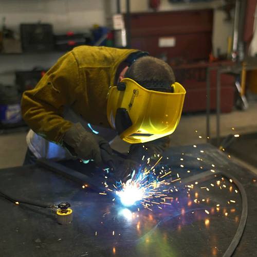 Welder using protective gear and a magnetic welding ground clamp with sparks flying in an industrial workspace