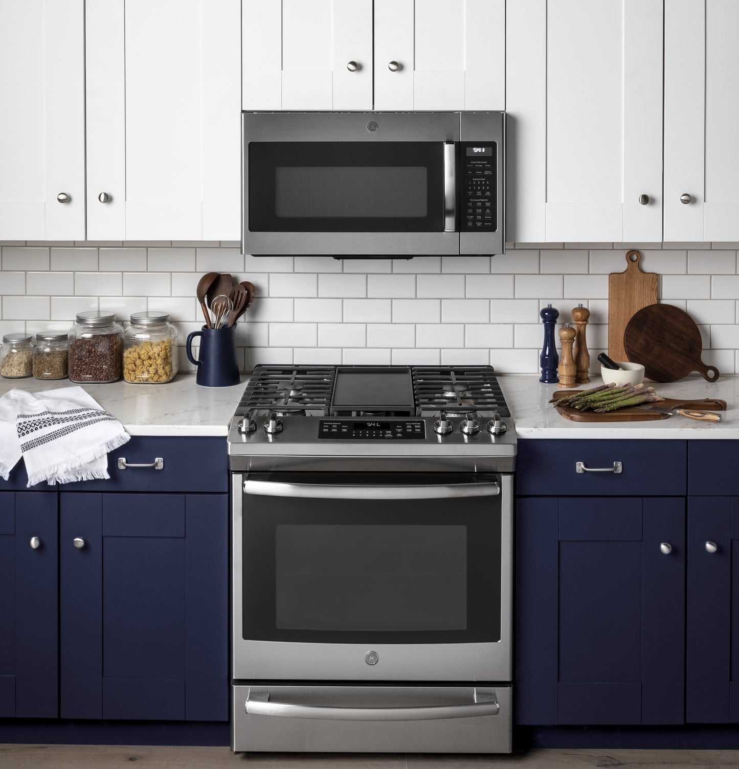 Stainless steel sensor microwave mounted above gas range with navy blue lower cabinets in kitchen setting
