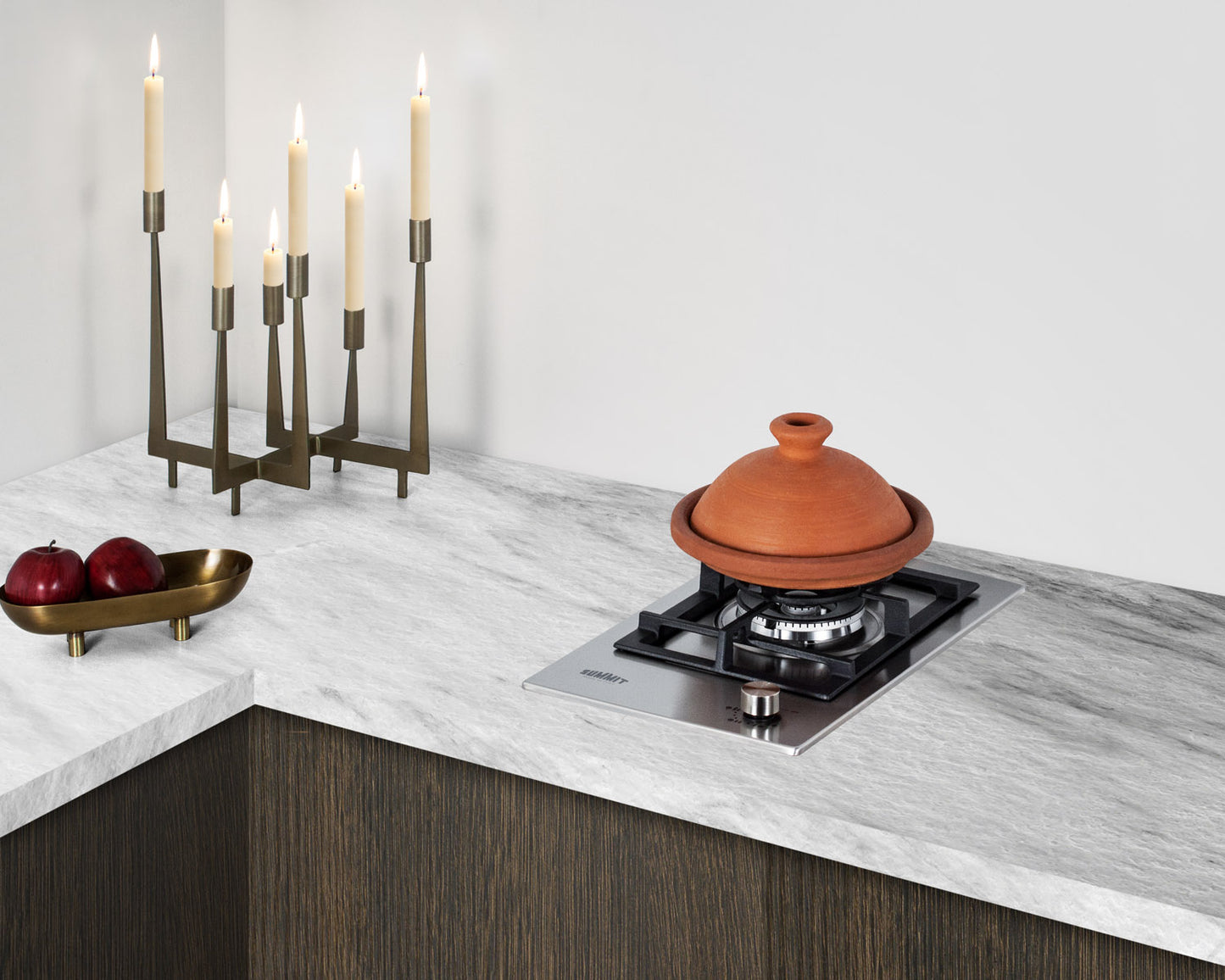 Stainless steel one-burner gas cooktop installed in modern kitchen countertop with lit candle holder and fruit bowl nearby