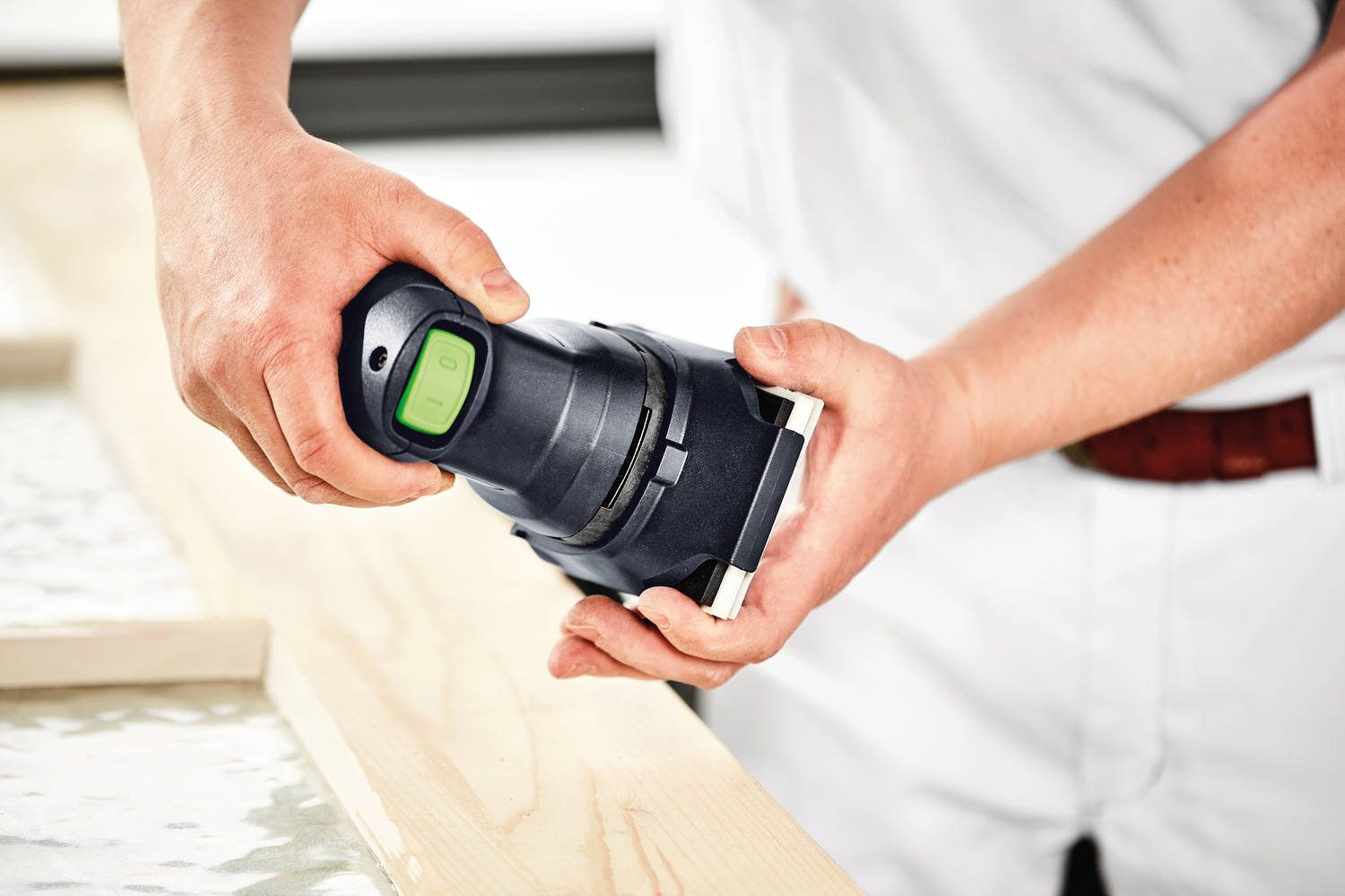 Person holding compact orbital finish sander with green power button, sanding wood edge for home improvement tasks