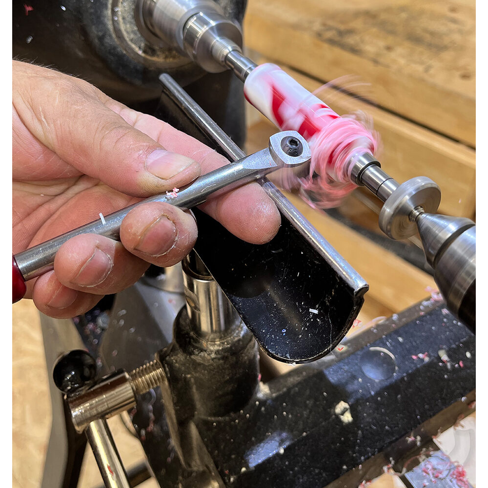 Hand using steel tool to shape red and white resin blank on lathe in woodworking tools under $100 collection
