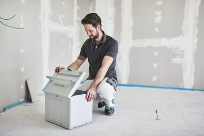 Man opening gray Festool tool storage box on unfinished room floor for jobsite workshop organization