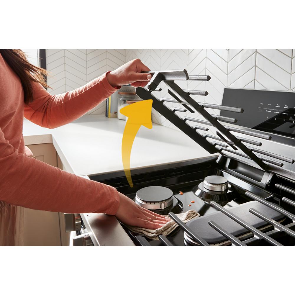 Person lifting dishwasher-safe hinged grate on gas range cooktop in modern kitchen appliances collection