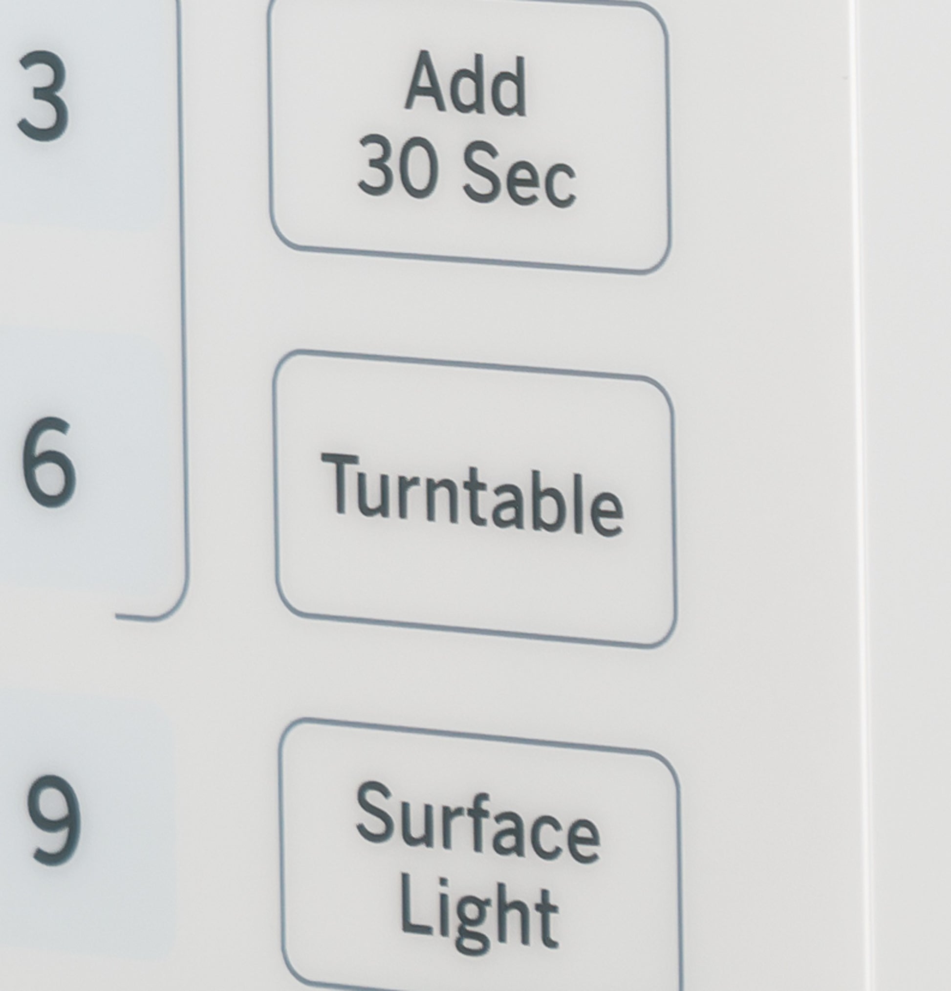 Close-up of white microwave oven control panel buttons for Add 30 Sec, Turntable, and Surface Light functions in kitchen appliance collection
