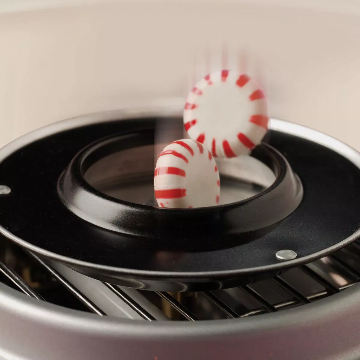 Two red-and-white striped hard candies spinning inside a black extractor head of a kitchen appliance