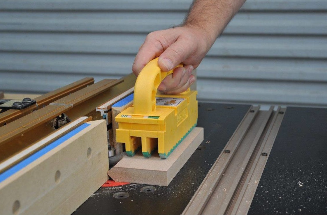 Hand pressing yellow Microjig GRR-RIPPER2 push block during safe wood cutting on table saw in tool accessories