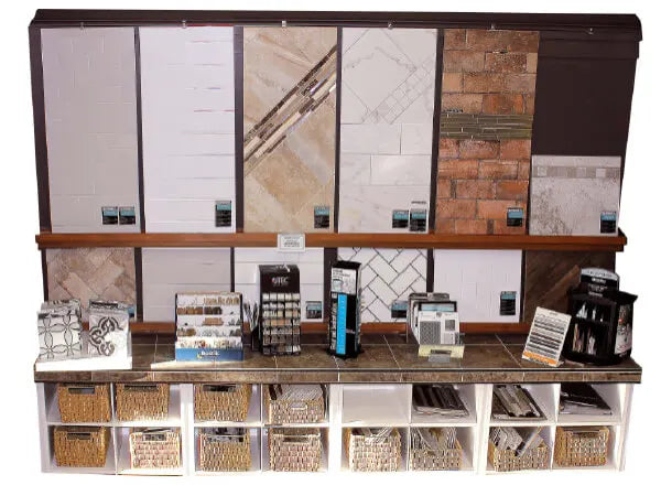 Display featuring a variety of tile and stone samples in different colors and patterns arranged on a dark stand with storage baskets underneath.