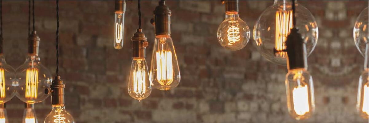 Variety of illuminated vintage-style Edison bulbs hanging from dark cords against a textured brick wall background, creating a warm ambiance.